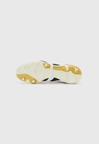 Black soccer cleat with a textured upper, white strap across the midfoot, and a white outsole featuring gold accents and studded spikes.