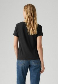 Camiseta de algodón negra con mangas cortas y escote redondo, combinada con unos vaqueros azul claros de talle alto con bolsillos traseros curvados.