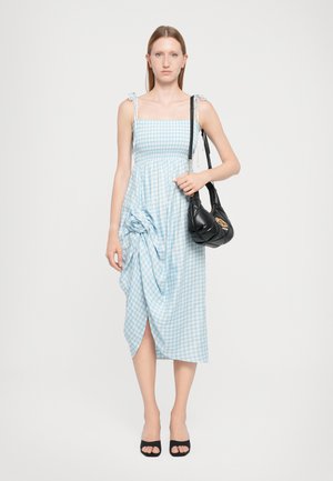Blue and white checkered dress with adjustable shoulder straps, wrapped design detail at the waist, and a thigh-high slit. Black handbag.