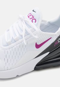 Bijela sportska tenisica s mrežastim gornjim dijelom, ljubičasti Nike logo, teksturirani detalji i crni zračni potplat. Rado su bijele i ravne.