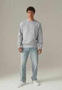 Grijze sweatshirt met ronde hals, gemaakt van katoen, met geribbelde manchetten. Gecombineerd met lichtblauwe spijkerbroek en witte sneakers. Casual pasvorm, zonder zichtbare patronen.