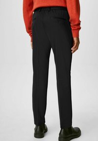 Svarta byxor med smal passform, resår i midjan och två bakfickor, kombinerade med en röd tröja och mörkgröna ankelboots.