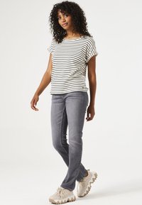Top de manga corta a rayas en crema y negro; combinado con jeans grises; el modelo lleva zapatillas gruesas en color beige. Cabello rizado, pose natural.