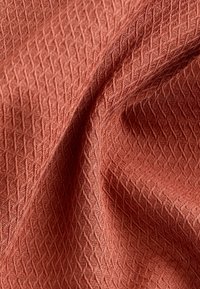 Textile fabric in a rust-orange color with a textured diamond pattern, showcasing intricate weaving details and a soft drape.