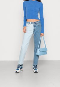 Maglione cropped a coste blu, jeans color block in denim chiaro e scuro, borsa blu, sneakers blu e bianche, con tessuto testurizzato e design strutturato.