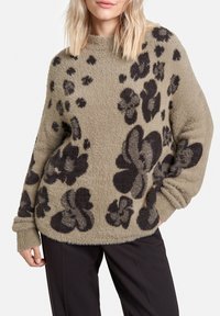 Pull en velours vert olive avec un grand motif floral noir, encolure ronde et coupe ample, avec des poignets et un ourlet côtelés.