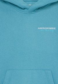 Hoodie turquoise en tissu doux, avec une poche frontale, capuche avec cordon de serrage, et texte brodé en blanc : "ABERCROMBIE New York City."