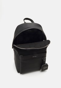 Black leather backpack with a zippered main compartment, front pocket, and detachable cardholder. Features a smooth texture and minimal branding.
