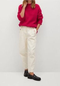 Maglione a maglia fucsia con collo rotondo, abbinato a pantaloni crema a vita alta con tasche frontali e dettagli di bottoni dorati. Mocassini neri.