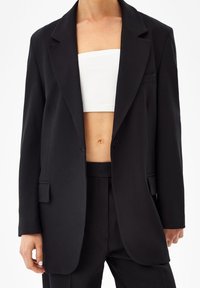 Svart skräddarsydd blazer med en strukturerad design, som har en enkel knappstängning, slagkragar och framfickor. Slät tygtextur.
