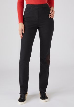Zwarte, getailleerde spijkerbroek met een hoge taille en vijf zakken. Gecombineerd met zwarte en beige sneakers. Glad textuur.