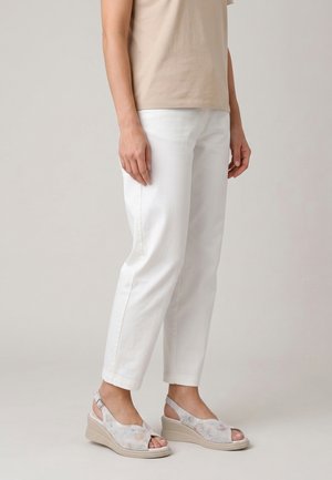 Personne portant un top beige, un pantalon droit blanc et des sandales compensées claires avec orteils ouverts et design perforé.