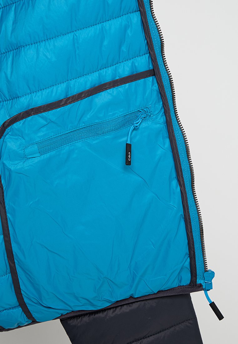 Interno di una giacca trapuntata blu che mostra una tasca con zip, con bordo nero e tirazip contrassegnato "CMP" su uno sfondo chiaro.