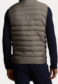 Mörkgrå puffertill med horisontella kviltade mönster och uppstående krage, bärs över en texturerad marinblå tröja. Dragkedjefickor synliga.