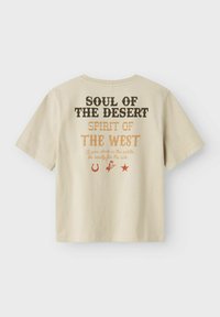 Krátký béžový bavlněný tričko s krátkými rukávy. Na zadní straně je vícbarevný text a ikony, včetně hvězd a podkovičky.