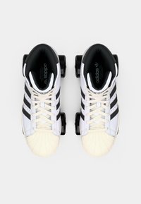 Λευκά πατίνια με μαύρες λεπτομέρειες, με τρεις μαύρες ρίγες, υφασμάτινους καπάκους από καουτσούκ και μαύρους τροχούς.