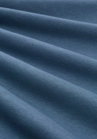 Tkanina bawełniana w głębokim niebieskim kolorze, charakteryzująca się gładką fakturą i subtelnym połyskiem, z widocznymi fałdami i jednolitym wzorem.