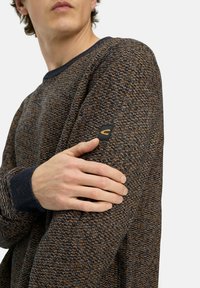 Gebreide trui in donkere blauw- en oranje tinten, met een textuurpatroon, geribde manchetten en een klein logo-opdruk op de mouw.