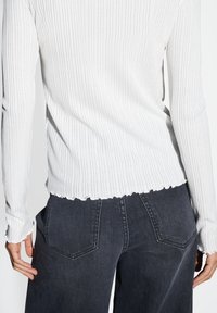 Weißes geripptes Langarmoberteil mit wellenförmigem Saum, kombiniert mit dunklen Jeans aus Denim mit klassischem Fünf-Taschen-Design.
