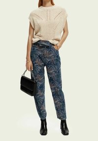 Pull beige en tricot à manches courtes avec un motif texturé, assorti à un pantalon bleu taille haute à motif feuillu, sac à main noir, bottines.