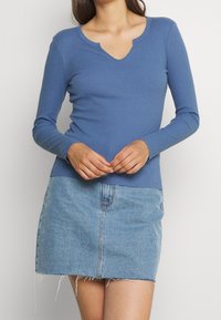 Maglietta a maniche lunghe a coste di colore blu con scollo a V e design aderente. Abbinata a una mini gonna in denim azzurro chiaro con orli sfilacciati.