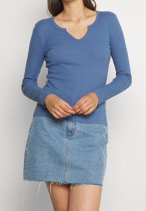 Maglietta a maniche lunghe a coste di colore blu con scollo a V e design aderente. Abbinata a una mini gonna in denim azzurro chiaro con orli sfilacciati.