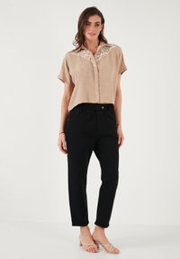 Chemise beige à manches courtes avec un col en dentelle, cinq boutons et un pantalon noir fuselé. Les sandales ont des fines lanières et un petit talon.