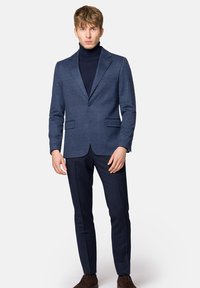 Granatowy garnitur z teksturowaną marynarką i dopasowanymi spodniami, z dopasowanym krojem, dwoma przednimi kieszeniami i ciemnym golfem pod spodem.