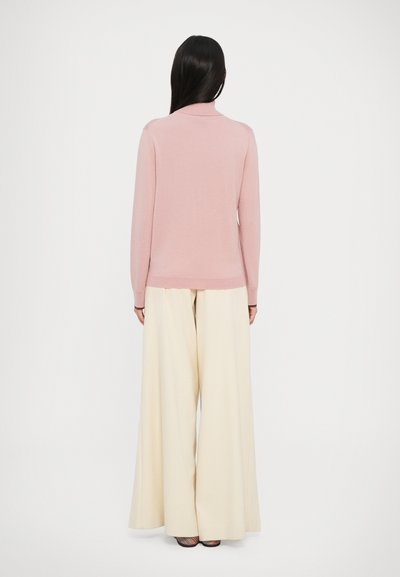 Maglione a maglia rosa chiaro con colletto alto, maniche lunghe e polsini a coste, abbinato a pantaloni ampi crema e sandali con tacco.