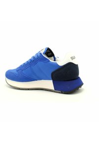Blauer Sneaker mit Obermaterial aus Mesh und Wildleder, weißer Fersenlasche, schwarzem Innenetikett und dicker Gummisohle mit grauen Akzenten.
