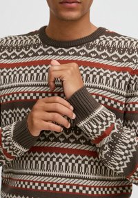 Pulover tricotat cu decolteu circular, cu o bază maro și un model geometric în alb, roșu și negru. Manșete și tiv cu insertie ribbed.