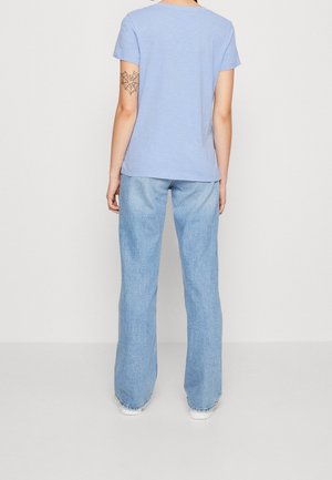 Camiseta de manga corta azul claro combinada con jeans de denim de lavado claro, sueltos, que cuentan con dobladillos deshilachados y un ajuste relajado.