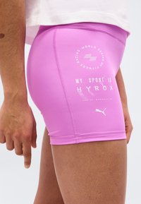 Άτομο που φοράει στενά ροζ αθλητικά σορτς με λευκό κείμενο και το λογότυπο της Puma στον μηρό που γράφει "Το άθλημά μου είναι HYROX."