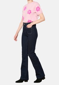 Suéter rosa de manga corta con aplique floral y pantalones vaqueros acampanados azul oscuro. Botines negros de tobillo completan el atuendo.