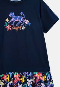 Tricou bleumarin cu mâneci scurte, decorat cu un imprimeu colorat cu tigru și flori în față, completat de un tiv cu volane cu un model.
