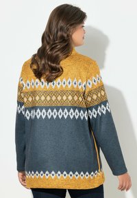 Pullover a maniche lunghe grigio e senape con motivi a diamante e geometrici. Texture morbida con vestibilità rilassata e spacchi laterali.
