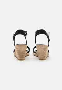 Sandalias de cuña de ante negro con tacón de yute trenzado, correa al tobillo con hebilla, parte trasera abierta y tiras delgadas en un diseño minimalista.
