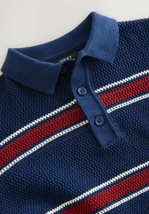 Polo shirt blu navy con un tessuto a maglia texturizzato, caratterizzato da accenti a righe rosse e bianche, due bottoni blu e colletto. Etichetta del marchio visibile.