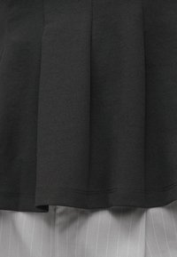 Czarna plisowana tkanina na jasnoszarej tkaninie z cienkimi białymi pionowymi pasami, ukazująca fakturę i szczegóły szycia.