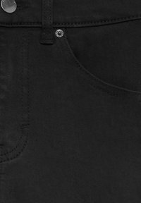 Gros plan sur la poche d’un jean en denim noir montrant les coutures, la boucle de ceinture et les rivets métalliques gravés de la marque.
