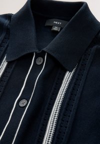 Polo de punto azul marino con cuello, que presenta rayas blancas y costuras decorativas, dos botones negros en la tapeta.