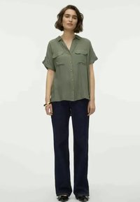 Olive green short-sleeve shirt with button front and two chest pockets, paired with dark blue wide-leg trousers and black shoes.