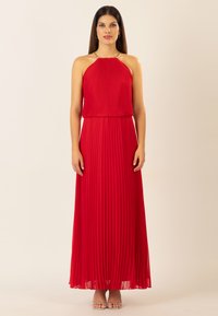 Rotes, plissiertes Maxikleid mit Halterneck und goldenen Hardware-Details. Fließender Stoff mit glatter Textur, getragen mit silbernen Sandalen.