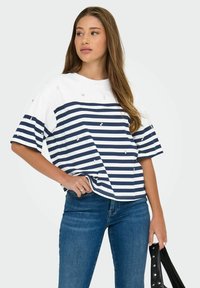 T-shirt à rayures à manches courtes en blanc et bleu marine, doté de rayures horizontales et de petits embellissements, associé à un jean bleu et un sac à main noir.