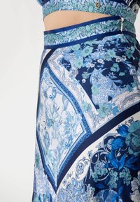 Jupe à motif floral bleu avec une taille ajustée. Présente un design géométrique, des nuances variées de bleu et une texture de tissu lisse et léger.