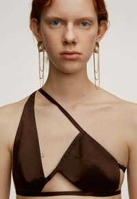 Top de bikini de satén marrón con un diseño asimétrico y tirantes entrecruzados. Pendientes de declaración en dorado con cadenas en capas completan el look.