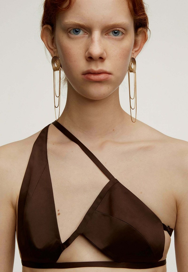 Top de bikini de satén marrón con un diseño asimétrico y tirantes entrecruzados. Pendientes de declaración en dorado con cadenas en capas completan el look.