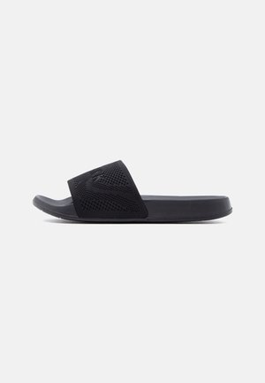 Sort slip-on sandal med tekstureret bred rem og flad sål, vist i sideprofil på en ensartet lys baggrund.