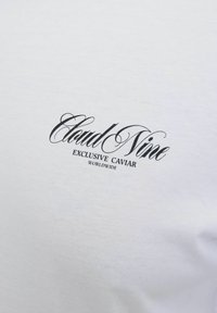 Valge puuvillane T-särk, millel on must script logoga kiri "Cloud Nine Exclusive Caviar" ning puhas ja sile tekstuur.