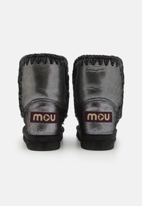 Botines negros brillantes al tobillo con acentos trenzados, que cuentan con un forro de felpa y un parche de marca en burdeos oscuro en la parte trasera.